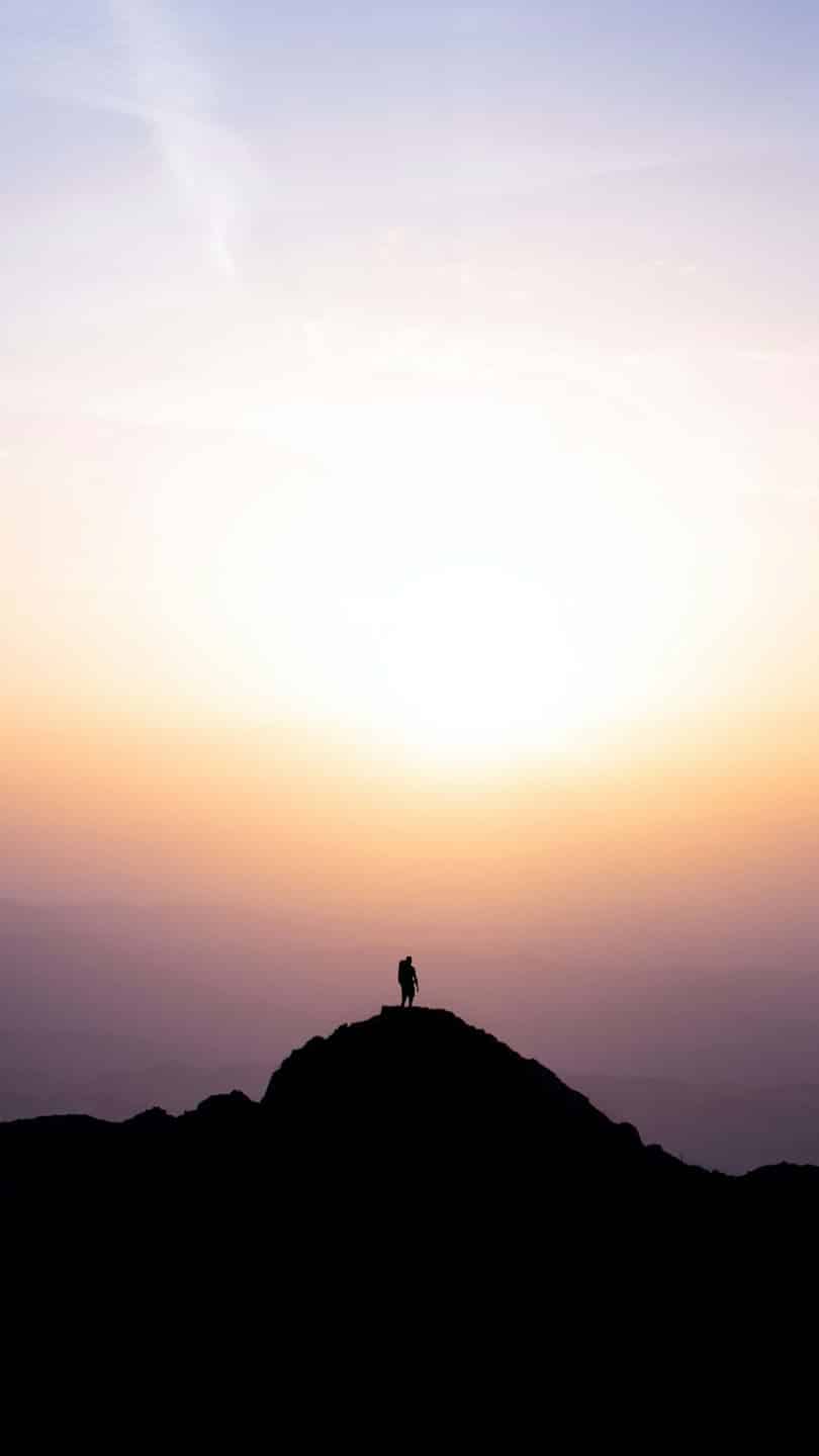 Escursionista in silhouette sulla cima di una montagna all'alba.