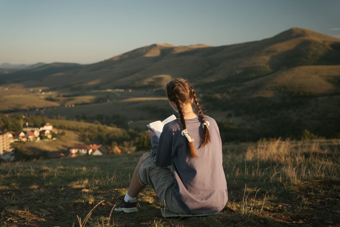 Persona che legge su una collina con vista su una valle al tramonto.